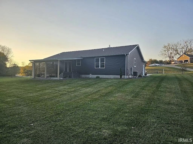 back house at dusk featuring central AC and a lawn