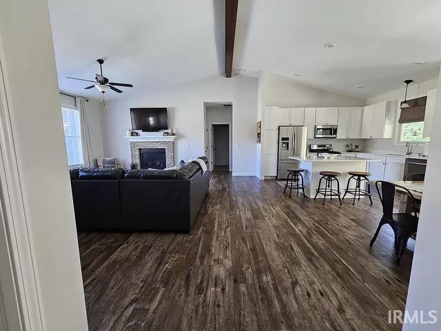 living room with ceiling fan, dark hardwood / wood-style floors, and vaulted ceiling with beams