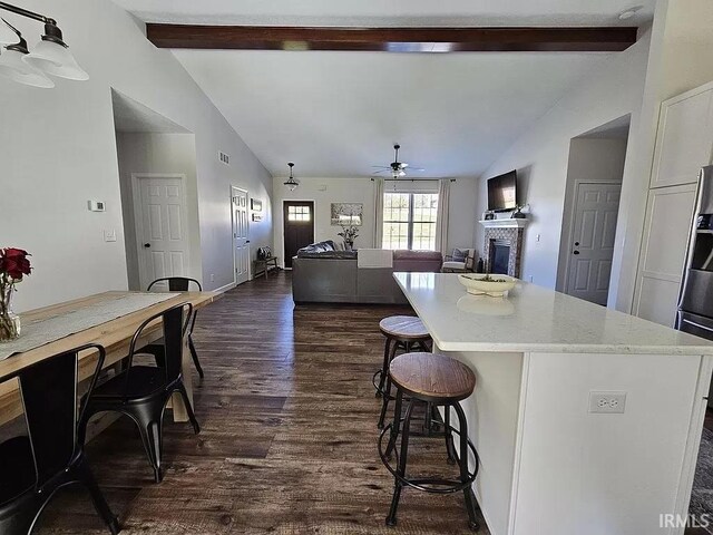 kitchen featuring a kitchen island, vaulted ceiling with beams, dark hardwood / wood-style flooring, ceiling fan, and light stone countertops