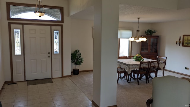 foyer entrance featuring a notable chandelier, plenty of natural light, light colored carpet, and a textured ceiling