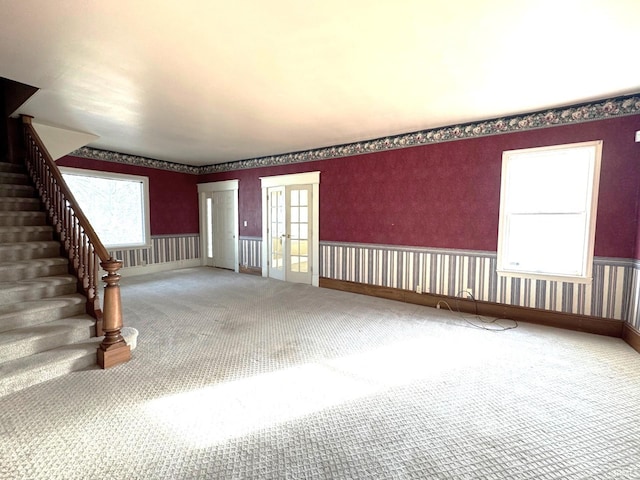 unfurnished living room with dark colored carpet, a healthy amount of sunlight, and french doors