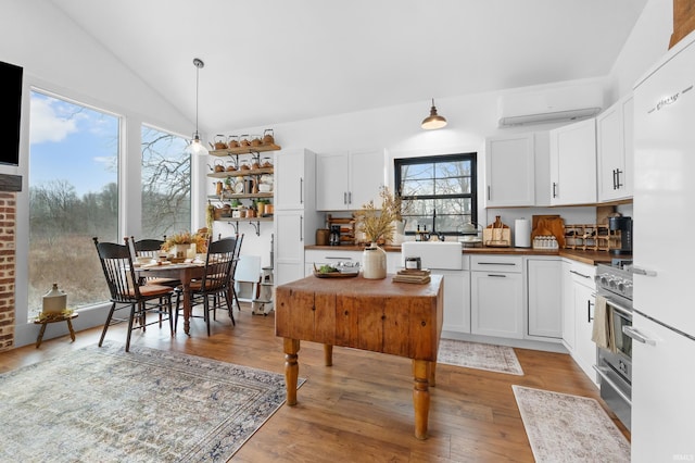 kitchen featuring lofted ceiling, hardwood / wood-style flooring, white cabinetry, hanging light fixtures, and a wall unit AC