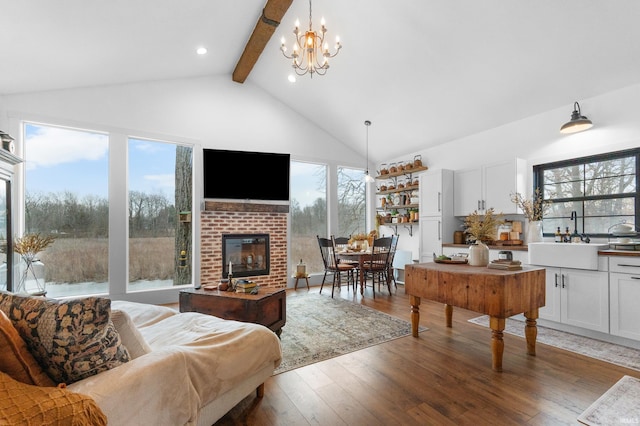 living room featuring sink, a notable chandelier, beamed ceiling, a fireplace, and hardwood / wood-style floors