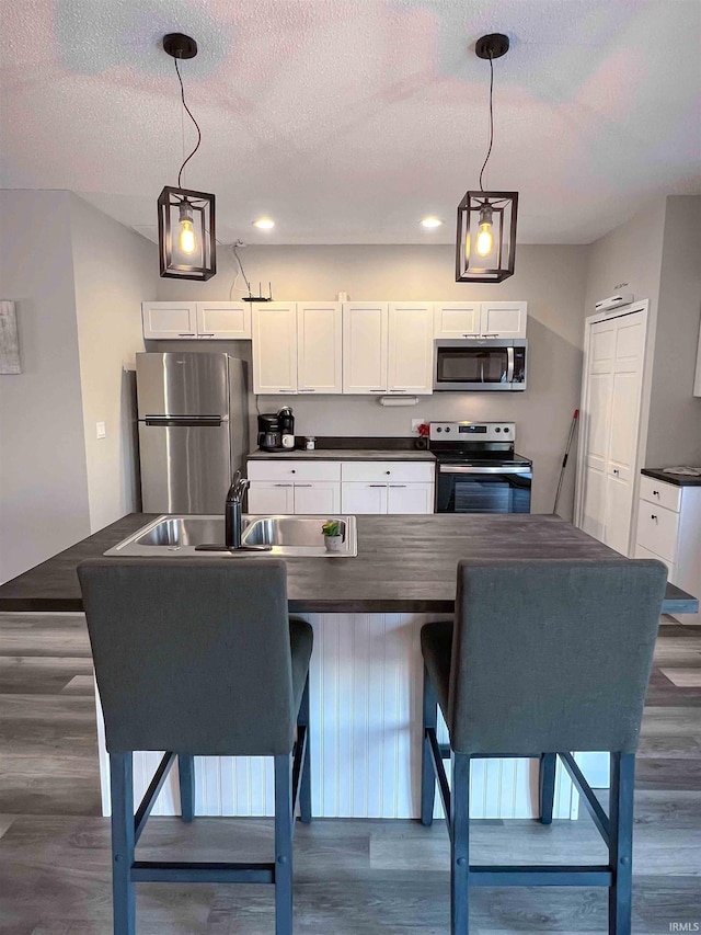 kitchen with dark hardwood / wood-style floors, decorative light fixtures, white cabinetry, sink, and stainless steel appliances