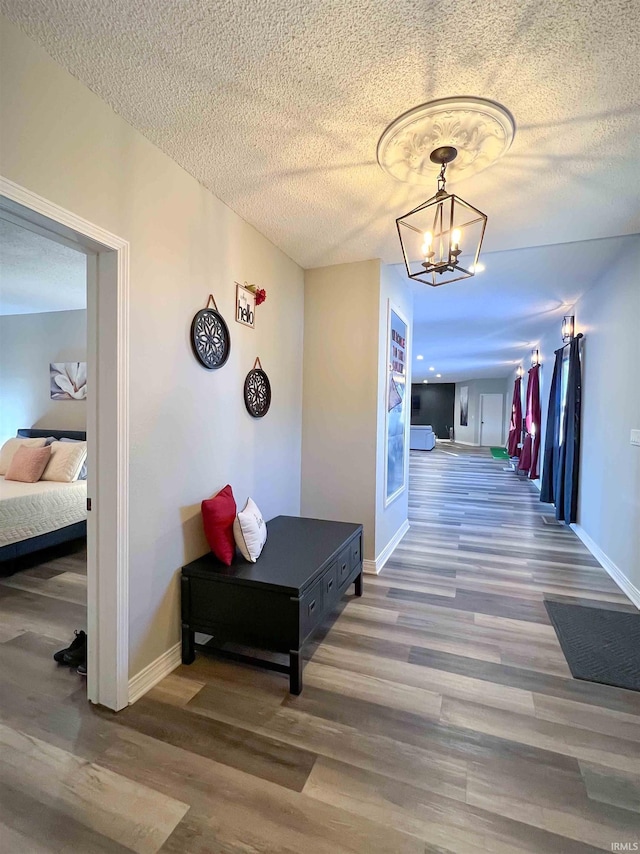 hallway with a notable chandelier, wood-type flooring, and a textured ceiling