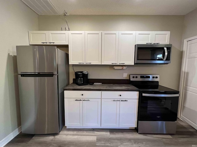 kitchen featuring stainless steel appliances, light hardwood / wood-style floors, a textured ceiling, and white cabinets