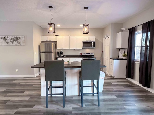 kitchen featuring white cabinetry, decorative light fixtures, a breakfast bar area, and stainless steel appliances