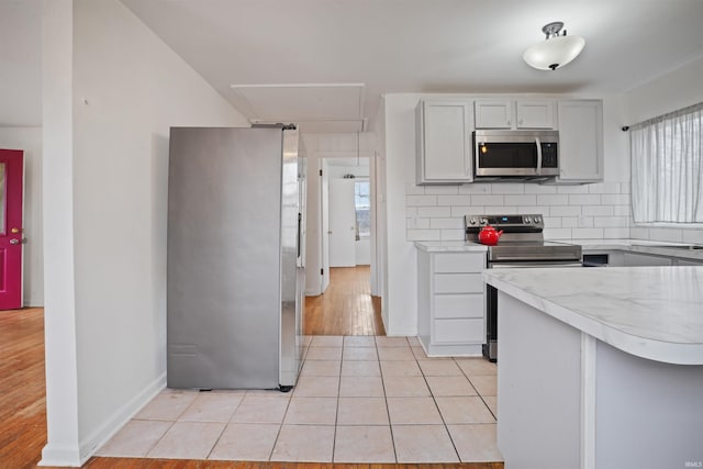 kitchen featuring backsplash, appliances with stainless steel finishes, kitchen peninsula, and light tile patterned floors