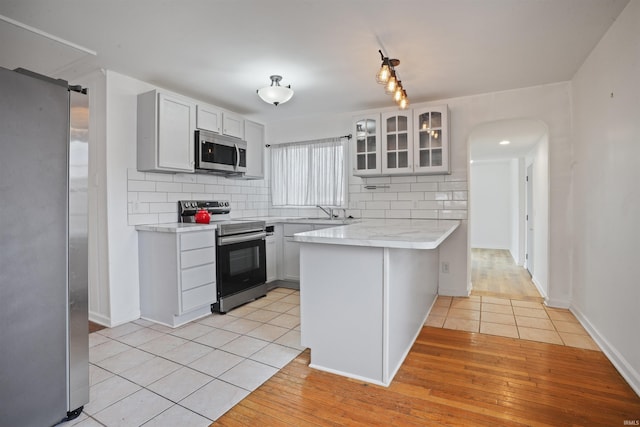 kitchen featuring appliances with stainless steel finishes, tasteful backsplash, white cabinets, kitchen peninsula, and light wood-type flooring