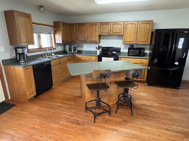 kitchen with a kitchen island, sink, a kitchen bar, hardwood / wood-style flooring, and black appliances