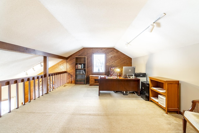 office area featuring vaulted ceiling, rail lighting, light colored carpet, and wood walls