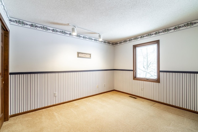 carpeted spare room featuring track lighting and a textured ceiling