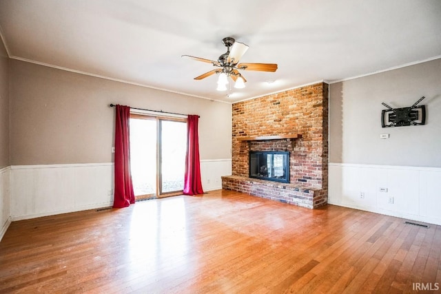 unfurnished living room featuring wood-type flooring, ornamental molding, ceiling fan, and a fireplace