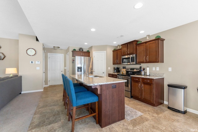 kitchen featuring sink, a kitchen breakfast bar, a kitchen island with sink, stainless steel appliances, and light stone countertops