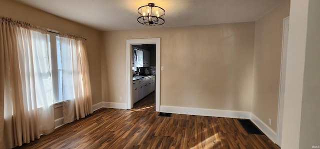 spare room with dark wood-type flooring, sink, and a notable chandelier