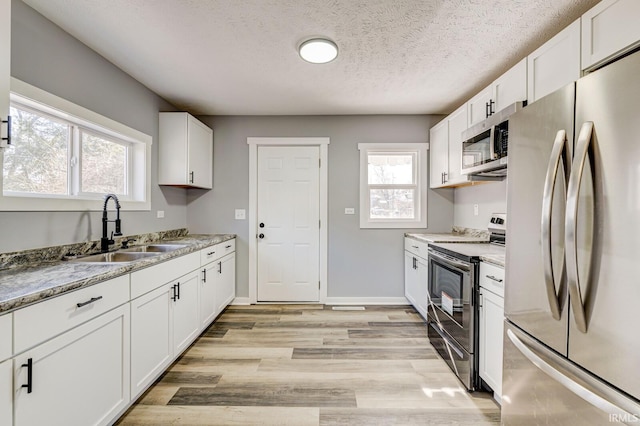 kitchen with sink, white cabinetry, light hardwood / wood-style flooring, appliances with stainless steel finishes, and light stone countertops