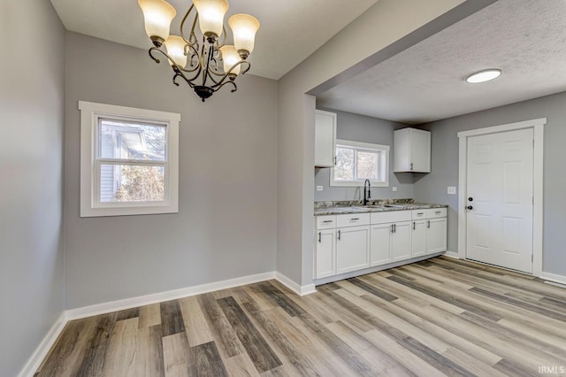 kitchen featuring light stone countertops, sink, pendant lighting, and white cabinets