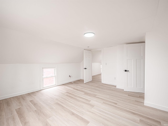 additional living space featuring baseboards, light wood-style flooring, and vaulted ceiling