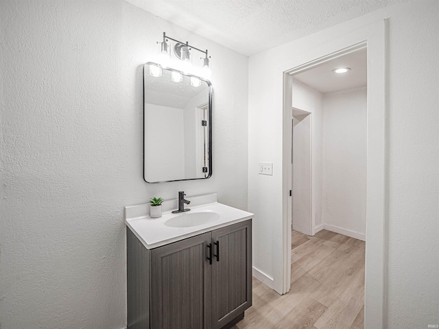 bathroom featuring vanity, wood finished floors, a textured ceiling, baseboards, and a textured wall