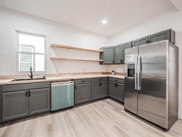 kitchen with light countertops, open shelves, gray cabinetry, a sink, and appliances with stainless steel finishes