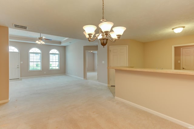 carpeted empty room with a tray ceiling and ceiling fan with notable chandelier