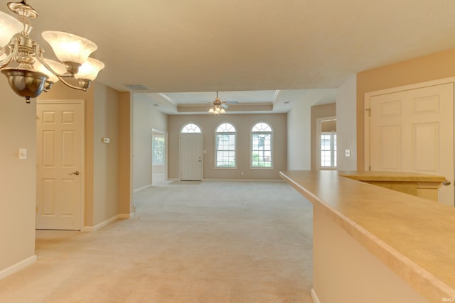 interior space with light colored carpet, a tray ceiling, and ceiling fan with notable chandelier