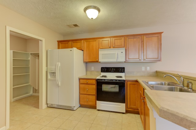 kitchen with sink, white appliances, light tile patterned floors, and a textured ceiling