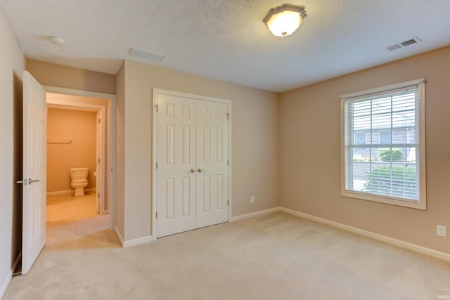 unfurnished bedroom with light colored carpet, a textured ceiling, and a closet