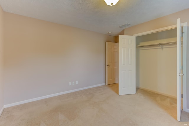 unfurnished bedroom featuring light colored carpet, a textured ceiling, and a closet