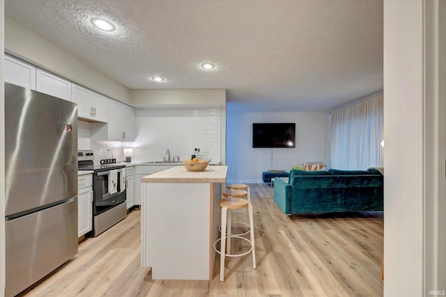 kitchen featuring a breakfast bar area, white cabinetry, butcher block counters, stainless steel appliances, and light hardwood / wood-style floors