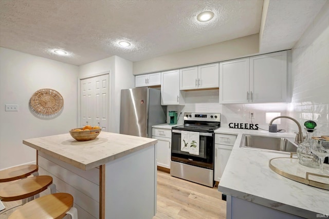 kitchen with sink, a center island, appliances with stainless steel finishes, light hardwood / wood-style floors, and white cabinets