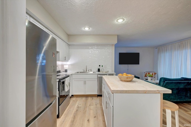 kitchen featuring appliances with stainless steel finishes, butcher block counters, a breakfast bar area, white cabinets, and sink