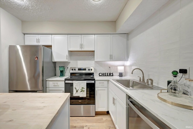 kitchen featuring sink, light hardwood / wood-style flooring, appliances with stainless steel finishes, white cabinets, and backsplash