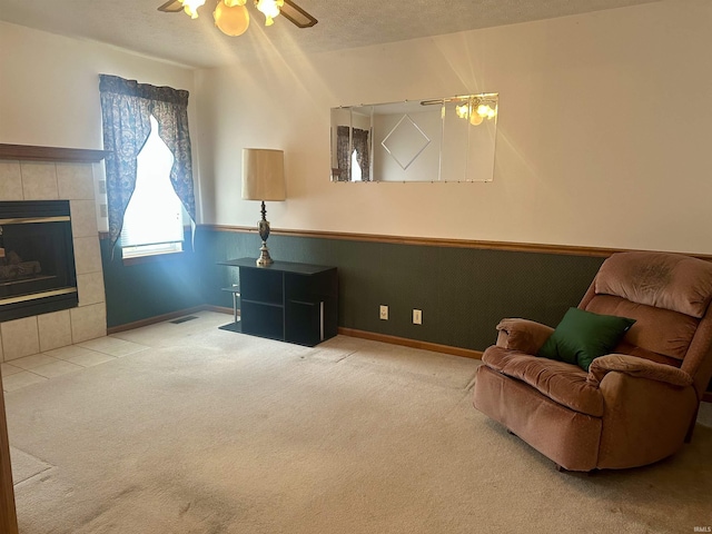 sitting room with a tiled fireplace, ceiling fan, carpet, and a textured ceiling