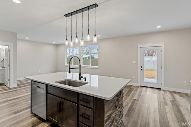 kitchen with sink, hanging light fixtures, light wood-type flooring, dishwasher, and a kitchen island with sink