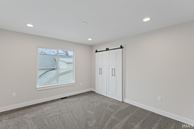 unfurnished bedroom featuring a barn door and carpet floors