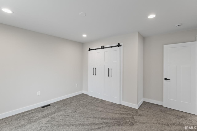 unfurnished bedroom featuring a barn door, carpet flooring, and a closet