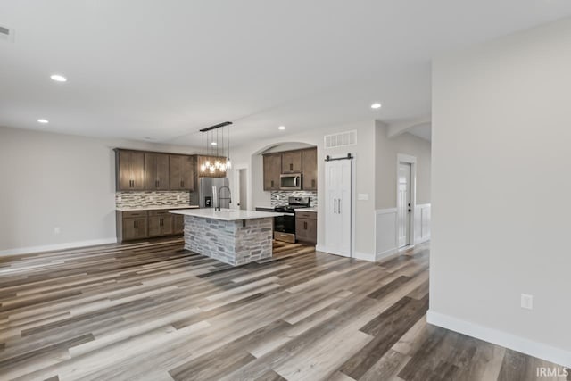 kitchen with pendant lighting, appliances with stainless steel finishes, tasteful backsplash, a center island with sink, and a barn door