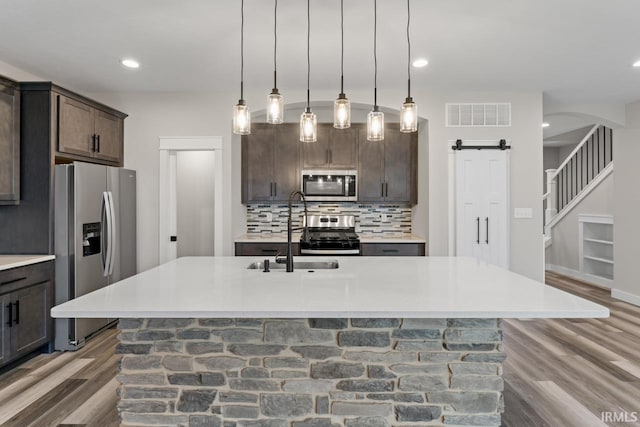 kitchen with dark brown cabinetry, appliances with stainless steel finishes, sink, and a center island with sink