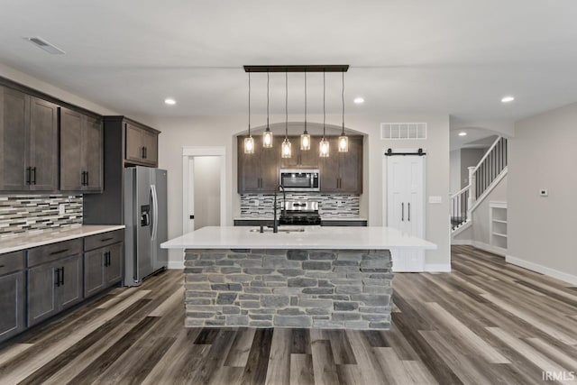 kitchen with dark brown cabinetry, sink, a center island with sink, appliances with stainless steel finishes, and a barn door