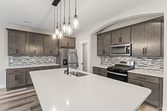 kitchen with pendant lighting, sink, dark brown cabinets, stainless steel appliances, and a center island with sink