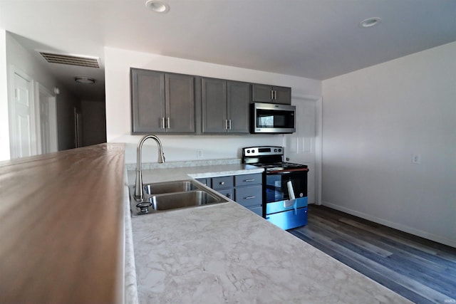 kitchen with appliances with stainless steel finishes, dark hardwood / wood-style flooring, sink, and gray cabinetry