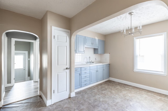 kitchen with sink, a notable chandelier, decorative backsplash, a textured ceiling, and decorative light fixtures