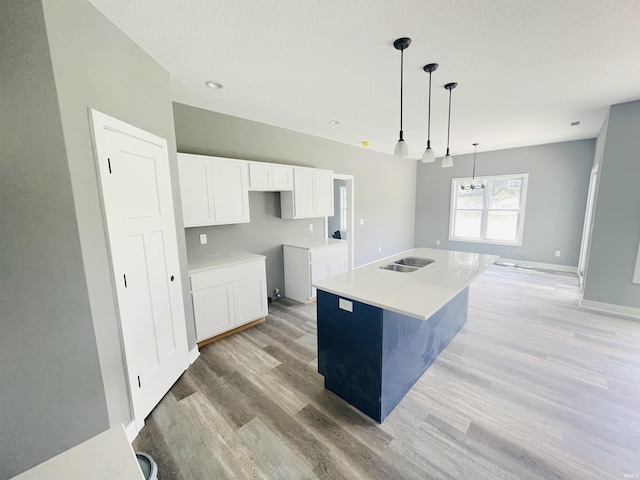 kitchen featuring sink, light hardwood / wood-style flooring, hanging light fixtures, a kitchen island with sink, and white cabinets