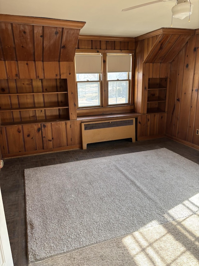 unfurnished living room with radiator heating unit, dark carpet, and wood walls