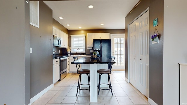 kitchen with black appliances, light tile patterned floors, a kitchen breakfast bar, a kitchen island, and white cabinets