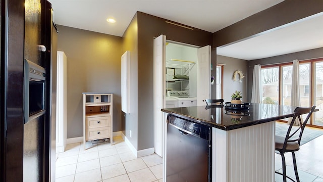 kitchen with light tile patterned floors, washer and clothes dryer, a kitchen breakfast bar, black appliances, and a kitchen island