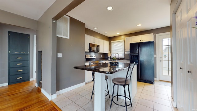 kitchen featuring white cabinetry, sink, a breakfast bar area, a center island, and black appliances