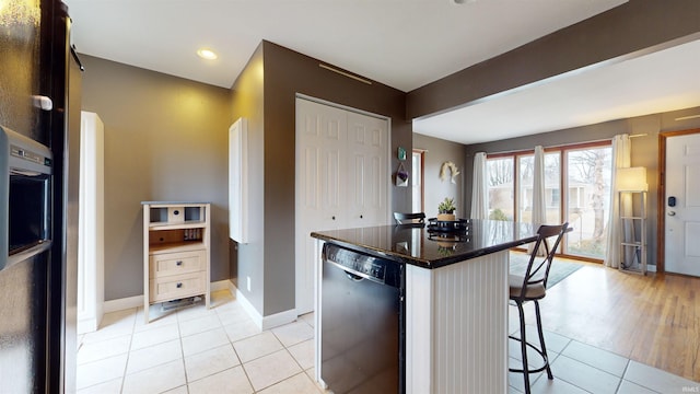 kitchen with a breakfast bar area, white cabinetry, a center island, light tile patterned floors, and dishwasher