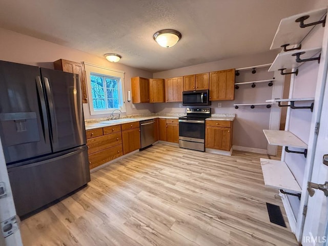 kitchen with stainless steel appliances, sink, light hardwood / wood-style flooring, and a textured ceiling